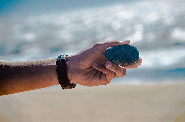 Hand holding a smooth stone by the beach on a sunny day.