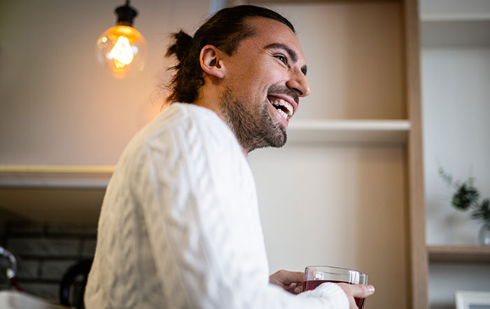 Man smiling joyfully indoors, holding a drink, exemplifying adorable things partners do.