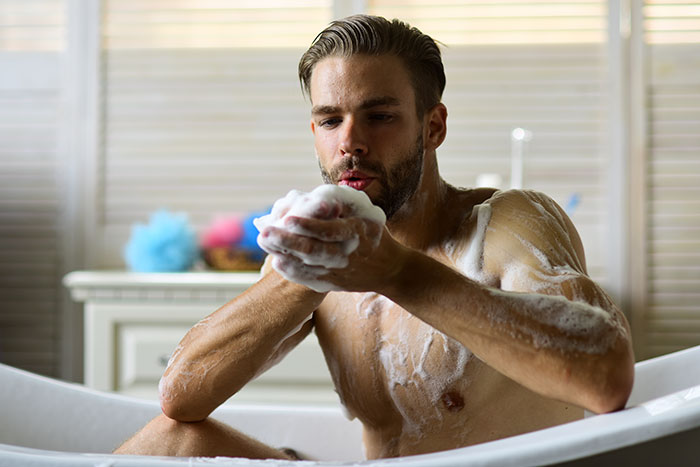 Man in a bathtub, playfully blowing soap bubbles, showcasing adorable actions partners do.