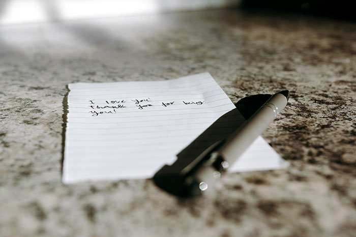 A handwritten love note from a partner on lined paper next to a silver pen on a countertop.