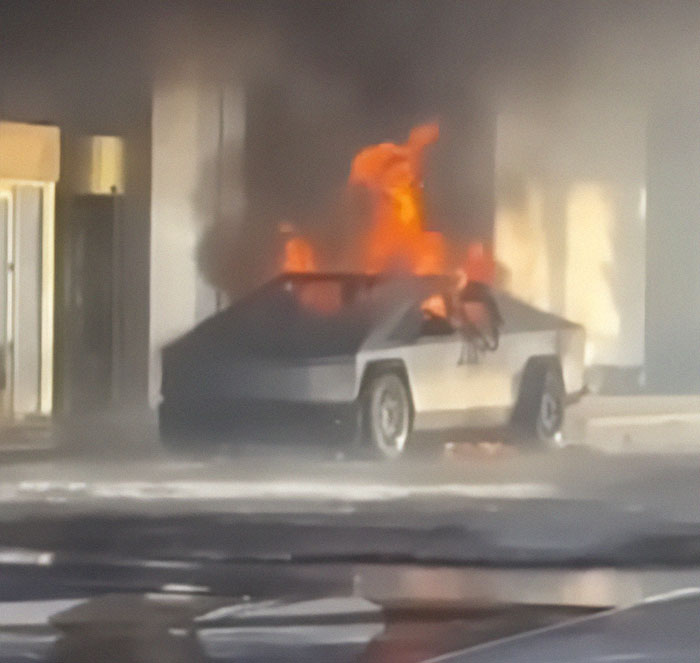 Cybertruck engulfed in flames outside a building, smoke rising from the explosion.