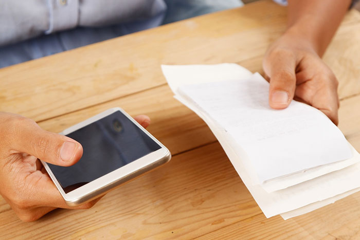 Person holding a phone and a receipt, illustrating unexpected vacation expenses.