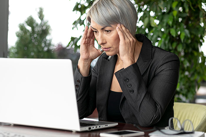 Woman in a suit looking stressed at a laptop, shocked by a hefty bill from a teen's vacation with a friend's family.