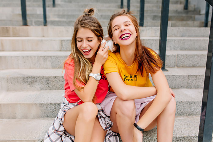 Two teens sitting on stairs, laughing and enjoying a vacation moment.