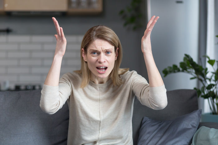 Frustrated woman on a couch reacting to daughter and boyfriend's senior trip plans.