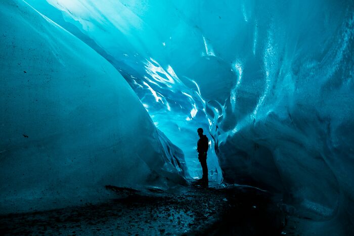 Person standing inside a stunning ice cave, showcasing natural phenomena with vibrant blue walls.