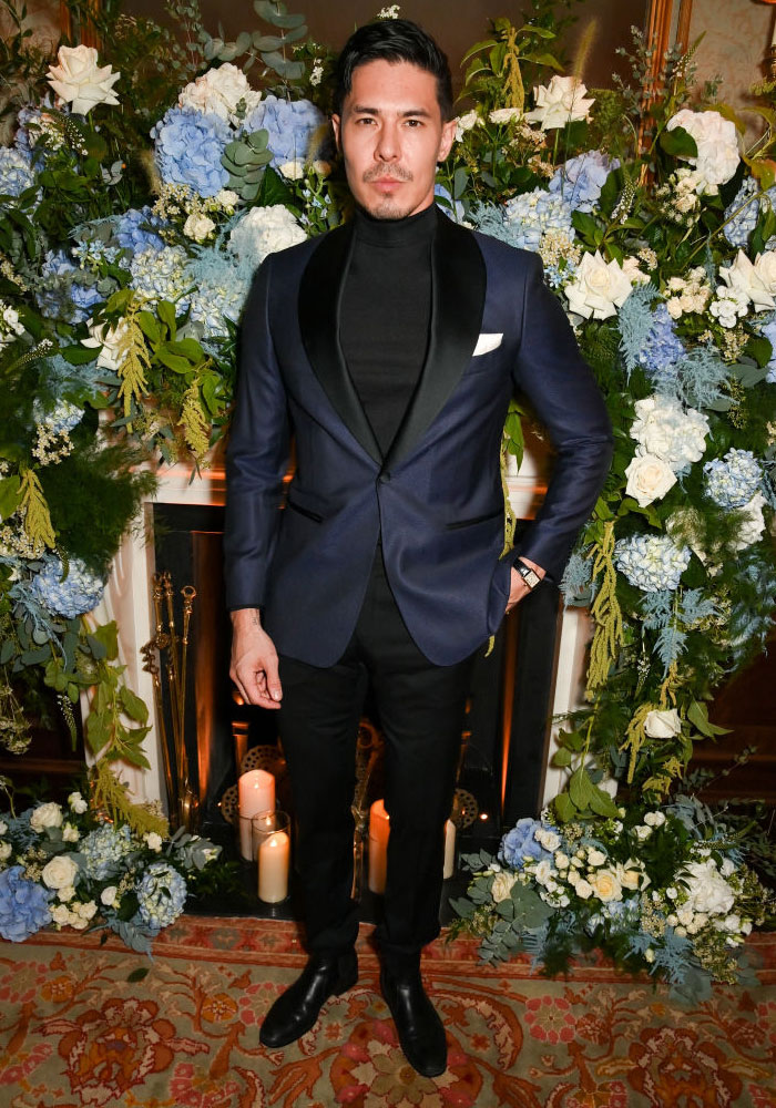 Lewis Tan in a blue suit standing by a floral arrangement, part of the Deadpool cast with surprising cameo potential.