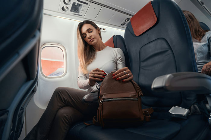 Woman seated on plane, holding a bag, exemplifying airline compassion and urgency to reach her terminally ill mother.