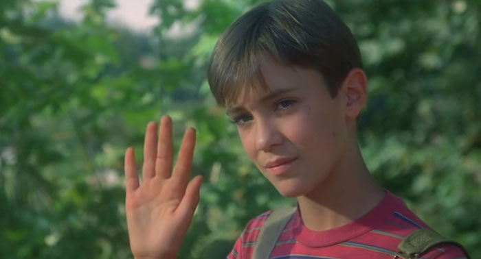 Young boy in striped shirt waving, scene from a movie with a sad ending.