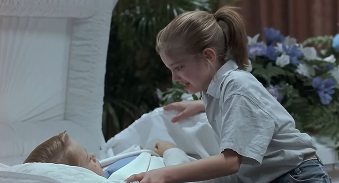 A young girl crying beside a casket, depicting a sad and depressing movie ending.