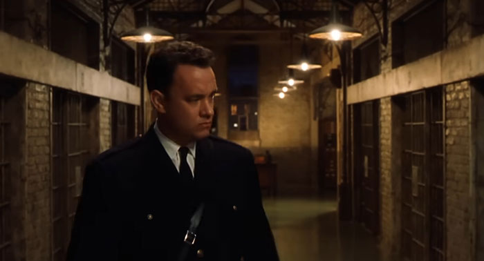 Prison guard walking down a dimly lit cell block, portraying a sad movie ending.