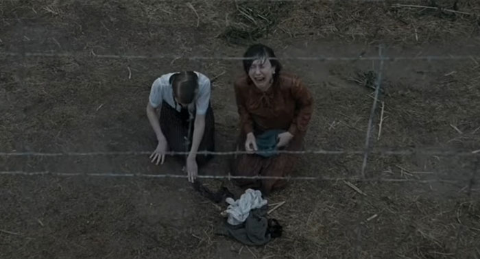 Two people kneeling near barbed wire on a dirt ground, conveying a sad and depressing movie ending.