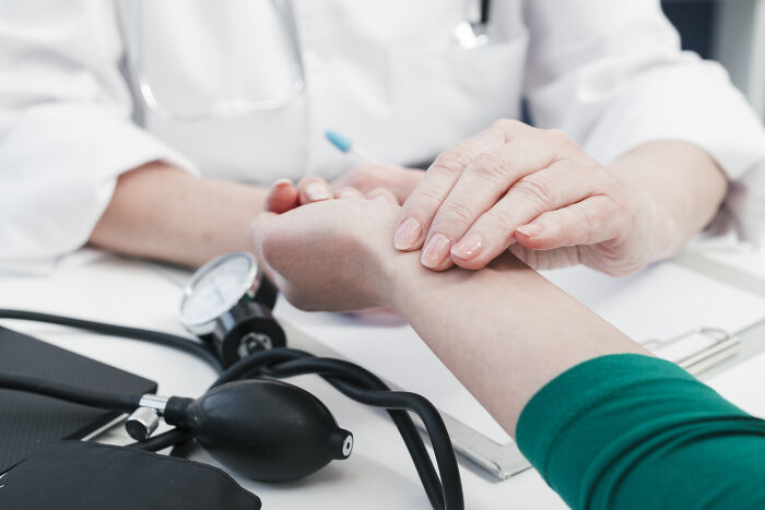 A doctor checking a patient's pulse with a blood pressure monitor, highlighting healthcare's increasing unaffordability.