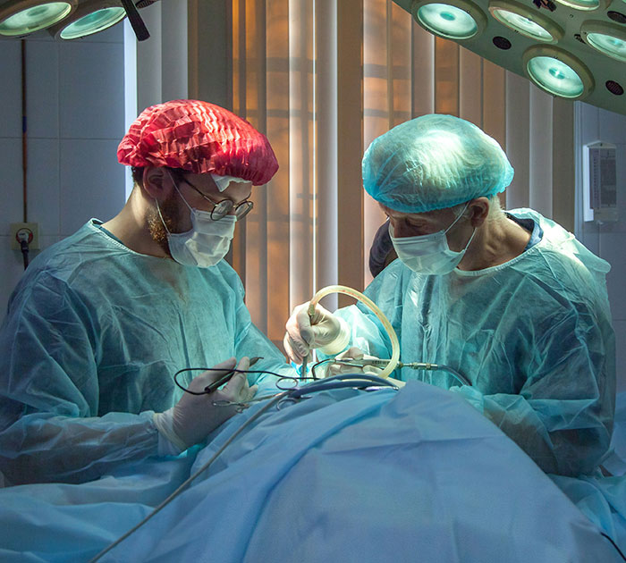 Surgeons in operating room wearing surgical gowns and caps, performing a medical procedure related to breast reduction.