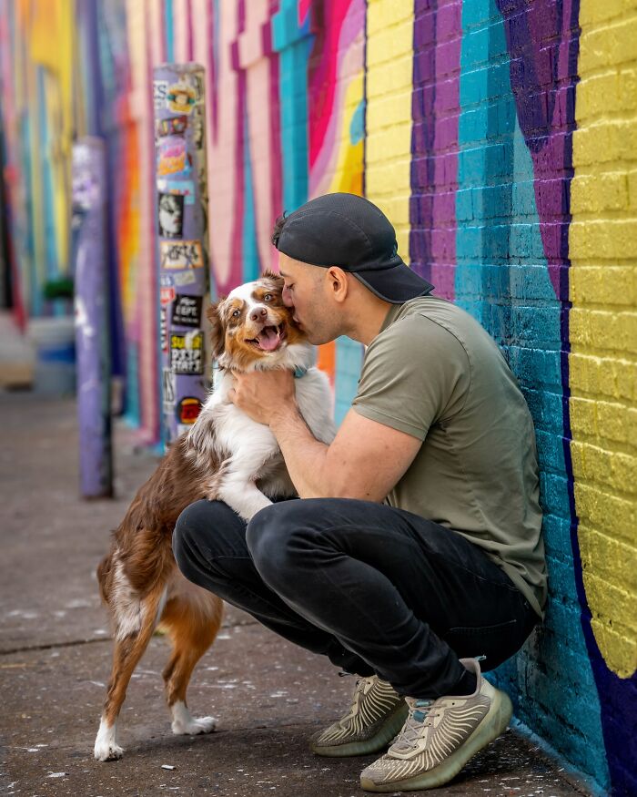 A man embraces a happy dog against a colorful NYC graffiti wall.