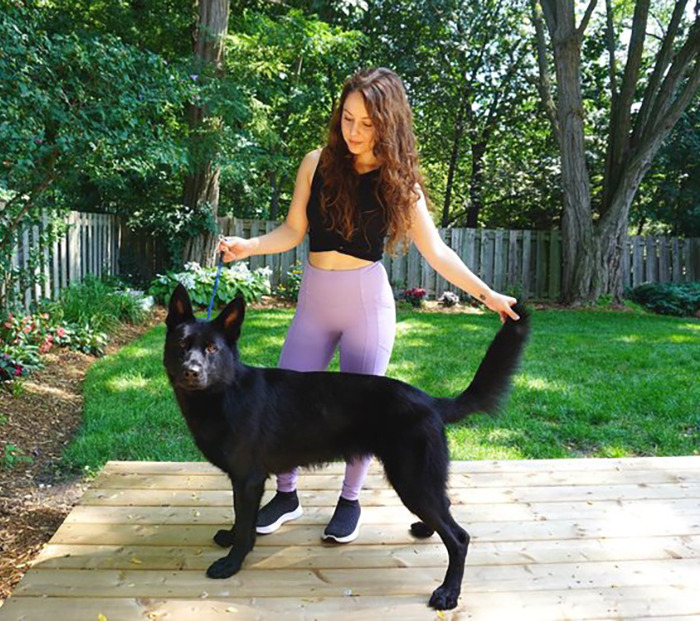 Vanessa De Prophetis with a black dog on a wooden deck in a lush backyard.