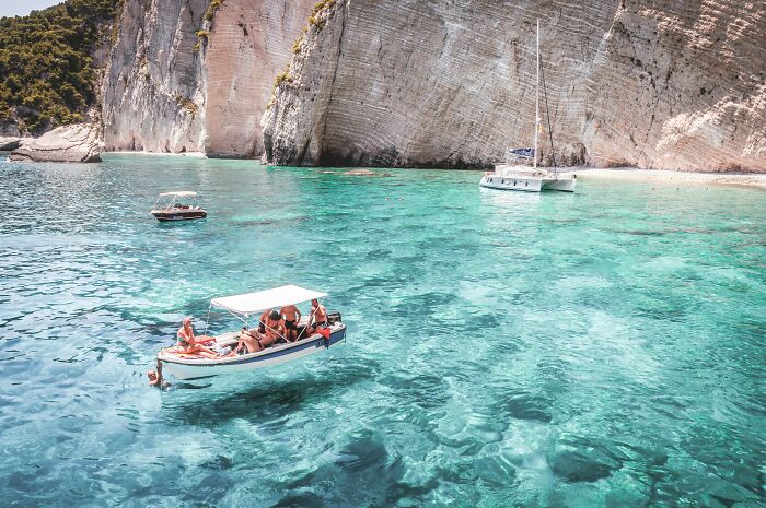 People enjoying a sunny boat trip in clear turquoise water near rocky cliffs.