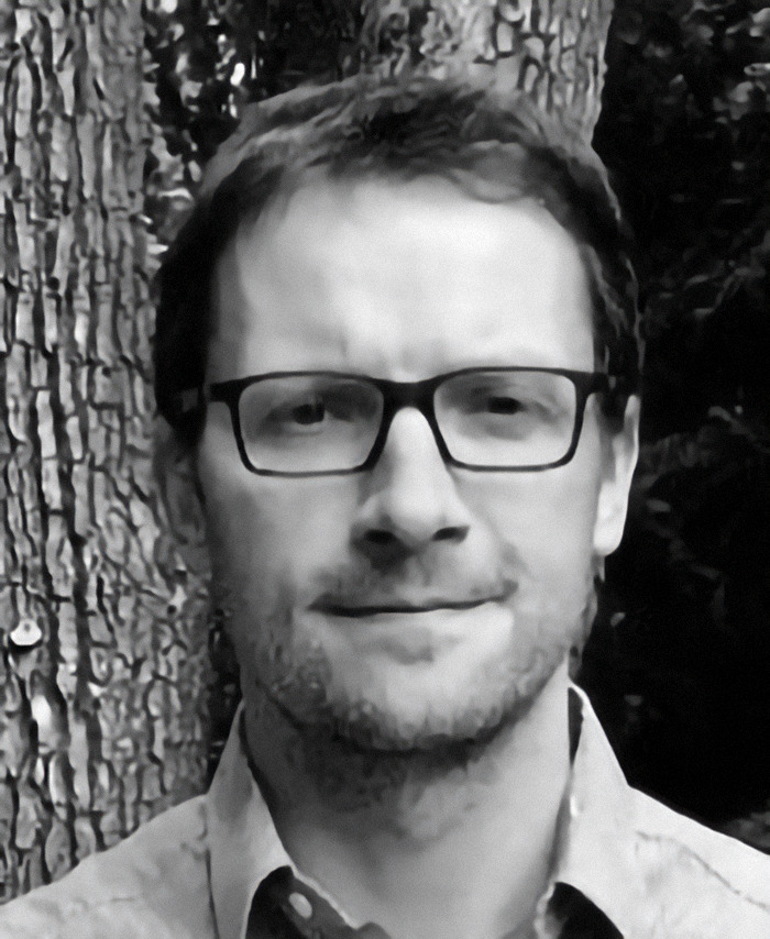 Edwin Nissen, Professor and Canada Research Chair in seismology at the University of Victoria, with glasses stands calmly outdoors in front of trees.