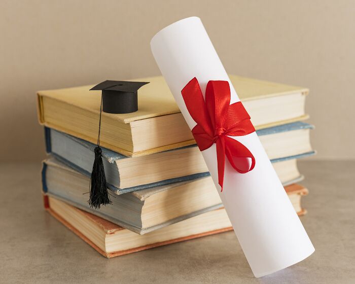 A graduation cap and diploma on stacked books, symbolizing education in context of the biggest scam in human history.