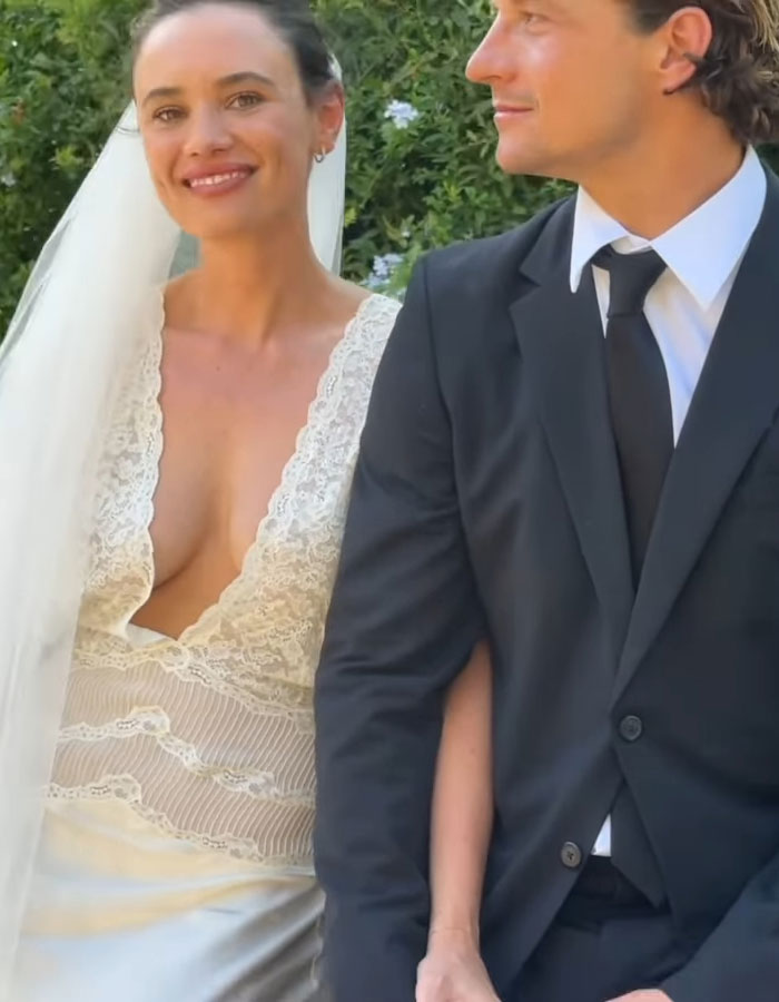 Australian bride in a lace wedding dress standing beside groom in a suit outdoors.