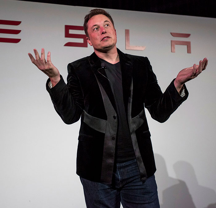 Man in a Tesla backdrop gesturing, discussing Cybertruck.