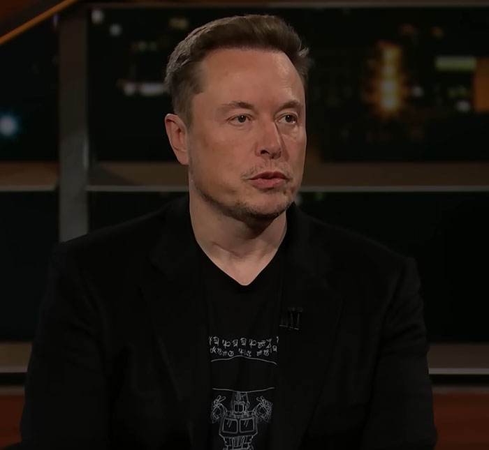 A man in a dark blazer sits on a talk show set.