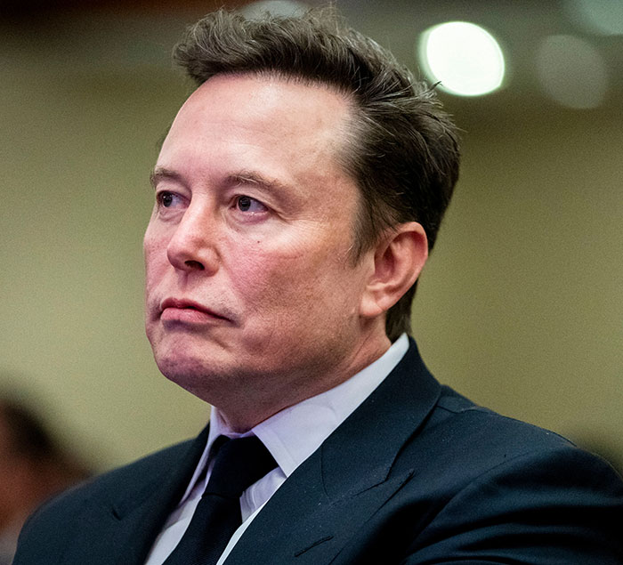 A man in a suit appears thoughtful at a public event, relevant to Cybertruck discussions.