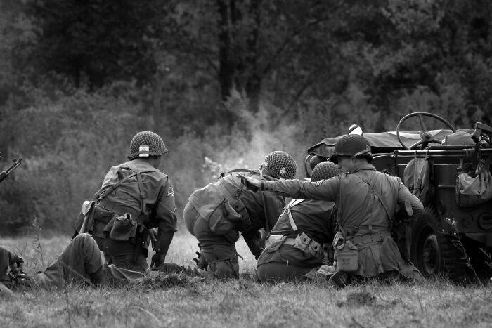 Soldiers in vintage uniforms beside a military vehicle in a grassy field, illustrating historical facts.