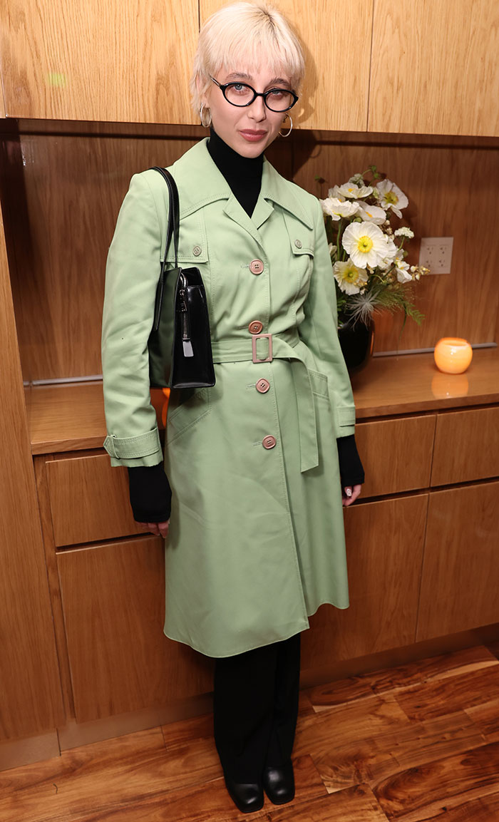 Emma Chamberlain in a mint green trench coat and glasses at Golden Globes after-party, labeled as a worst-dressed attendee.