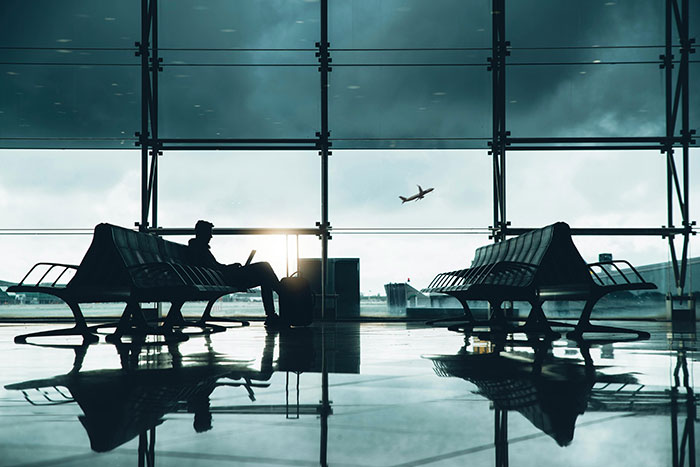 Silhouette of a person sitting in an airport terminal with a plane taking off outside.