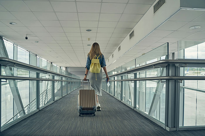 Woman with suitcase walking through airport terminal corridor.