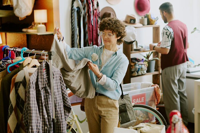 Person thrifting in a store, examining clothing items with enthusiasm.