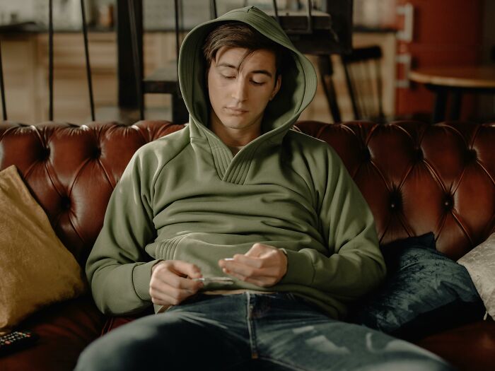 Person in a green hoodie sitting on a leather couch, representing a relaxed lifestyle amid rising costs.