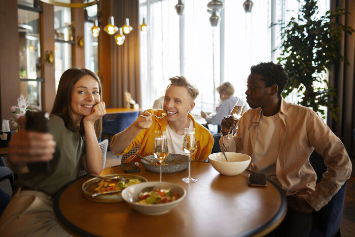 Three friends enjoying a meal together, discussing changes in spending on concerts and beauty luxuries.