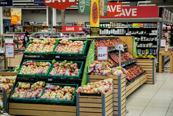 Grocery store aisle with fruits and signs highlighting savings amidst rising cost concerns.