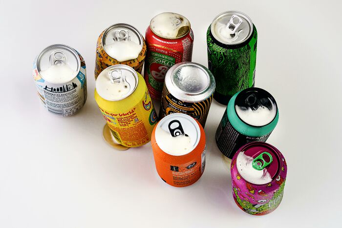 A variety of colorful soda cans viewed from above, suggesting luxury items people skip due to cost.