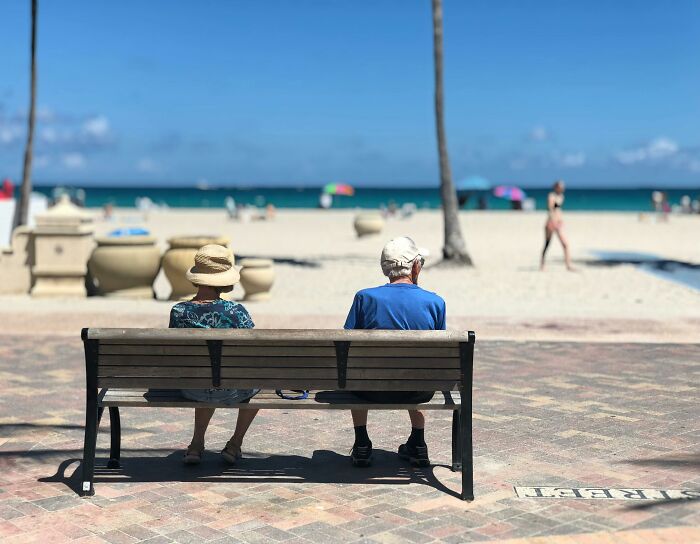 Two people sitting on a bench facing the beach.