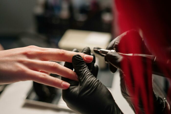 Nail technician wearing gloves manicures a client's hand, highlighting beauty luxuries.