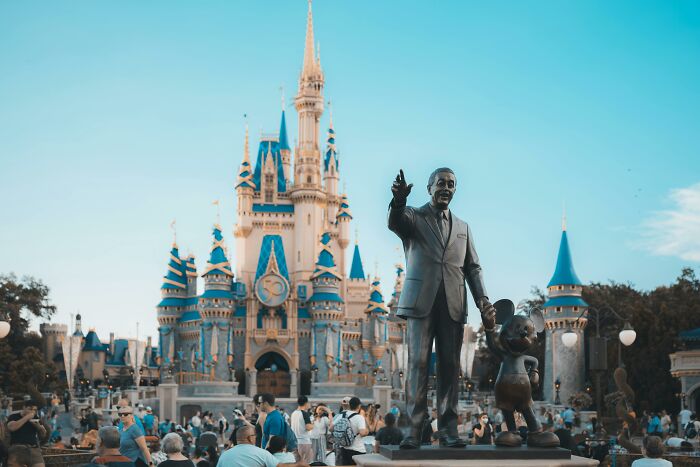 A crowded theme park with a castle and a statue, illustrating rising costs of entertainment and travel luxuries.