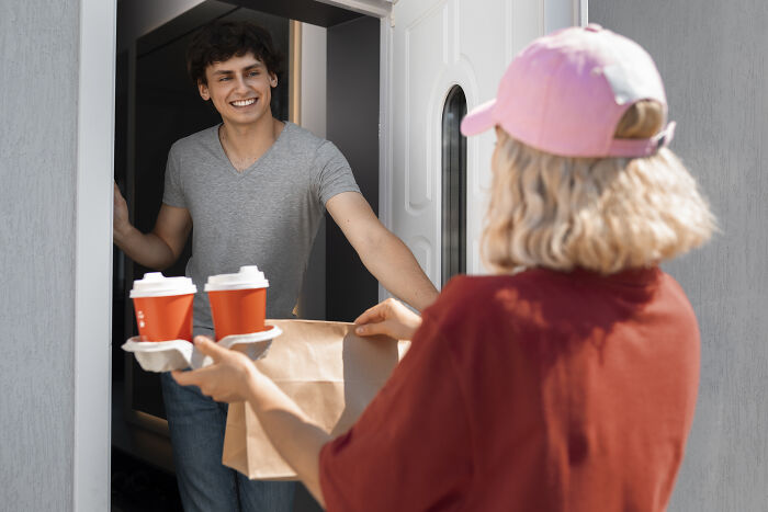 Person delivering coffee and a bag to someone at a doorway, highlighting cost-related lifestyle changes.