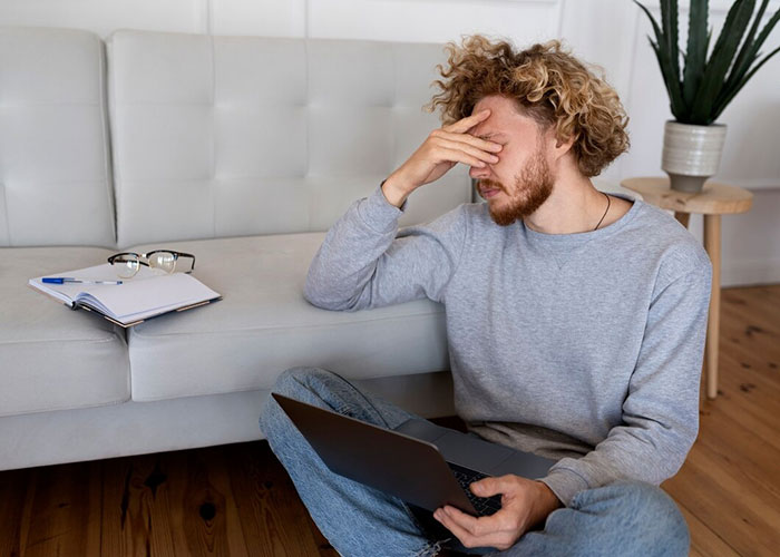 Man sitting by couch with laptop, looking concerned about missing from in-laws' anniversary collage.