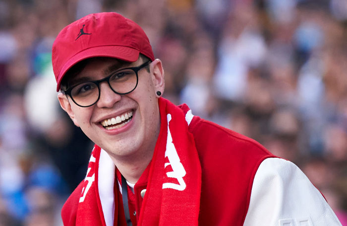 Streamer juansguarnizo (Juan Sebastian Guarnizo Algarra) in a red cap and jacket, smiling at an outdoor event.