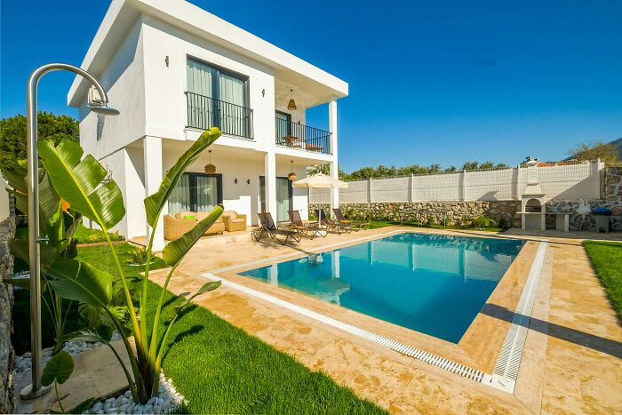 Modern house with a pool and patio, surrounded by greenery, under a clear blue sky.