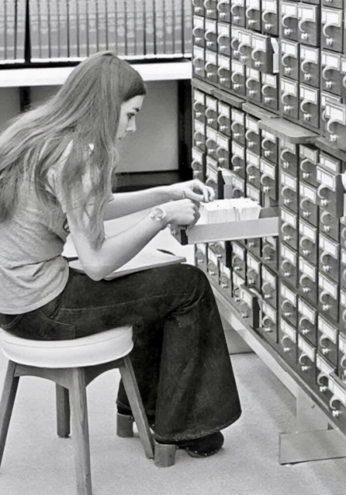 A woman explores a library card catalog, reflecting on fascinating historical research methods.