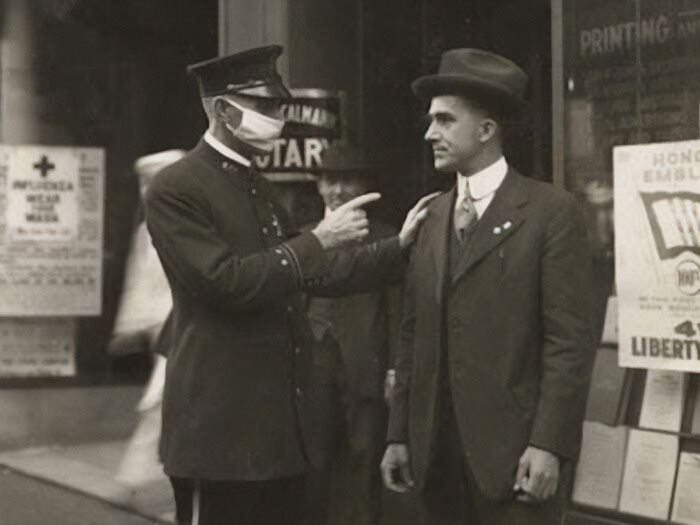 A masked policeman enforces influenza mask rules on a man in a vintage setting, capturing historical significance.