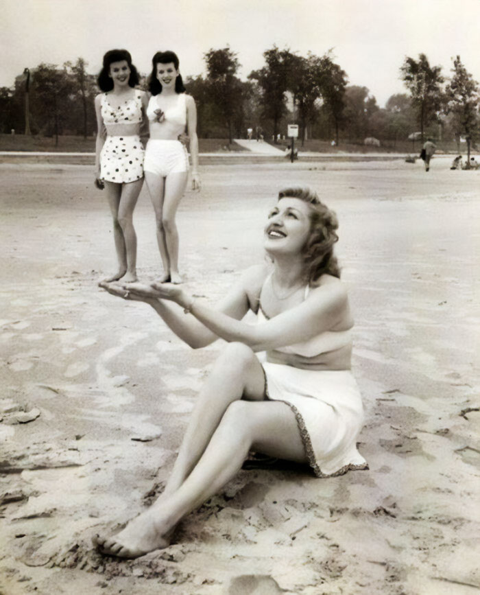 Vintage beach photo with creative perspective showing two women seemingly standing on another woman's hand.