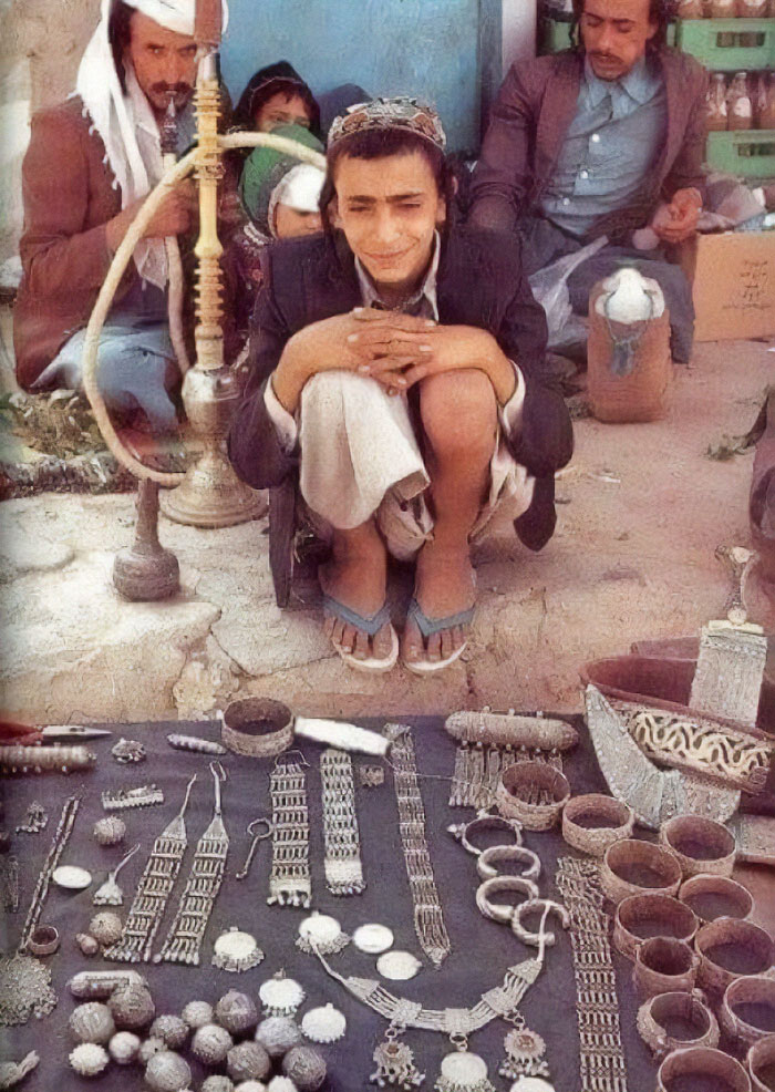 A man surrounded by historical jewelry and artifacts, smiling, with others in the background.