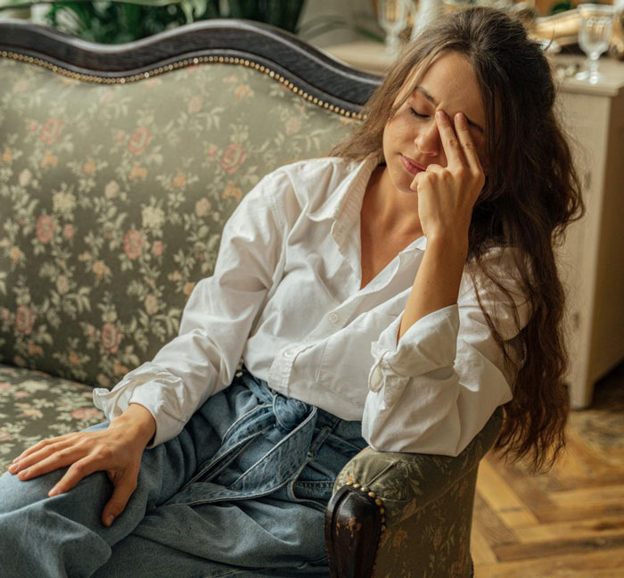 Woman in white shirt sits on floral sofa, looking pensive; theme of family, priority, and adoption discussed.