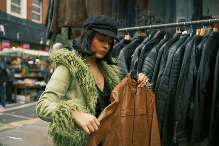 Woman in a green jacket browsing leather coats at an outdoor market.