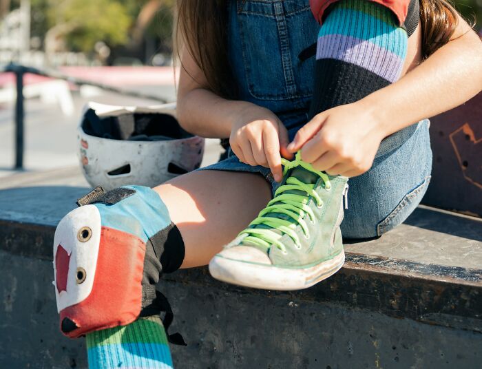 Close-up of a person in colorful knee pads and sneakers, lacing up shoes at a skate park.